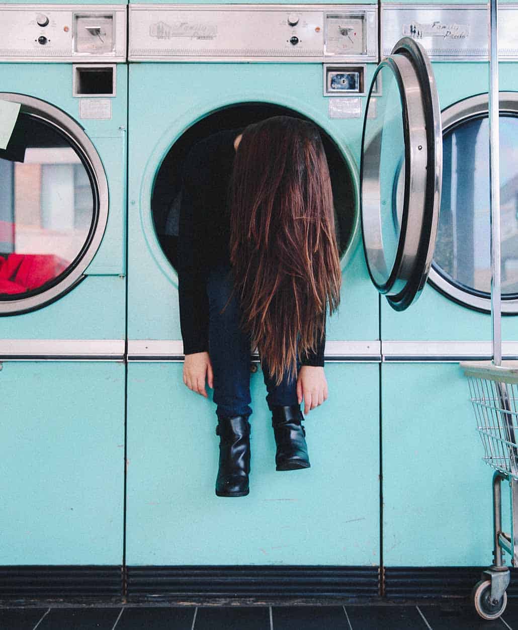 child sitting in blue washing machine hanging her legs and arms out while dangling head admitting defeat over head lice