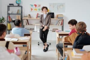 children sitting at desks facing teacher at the front of the classroom